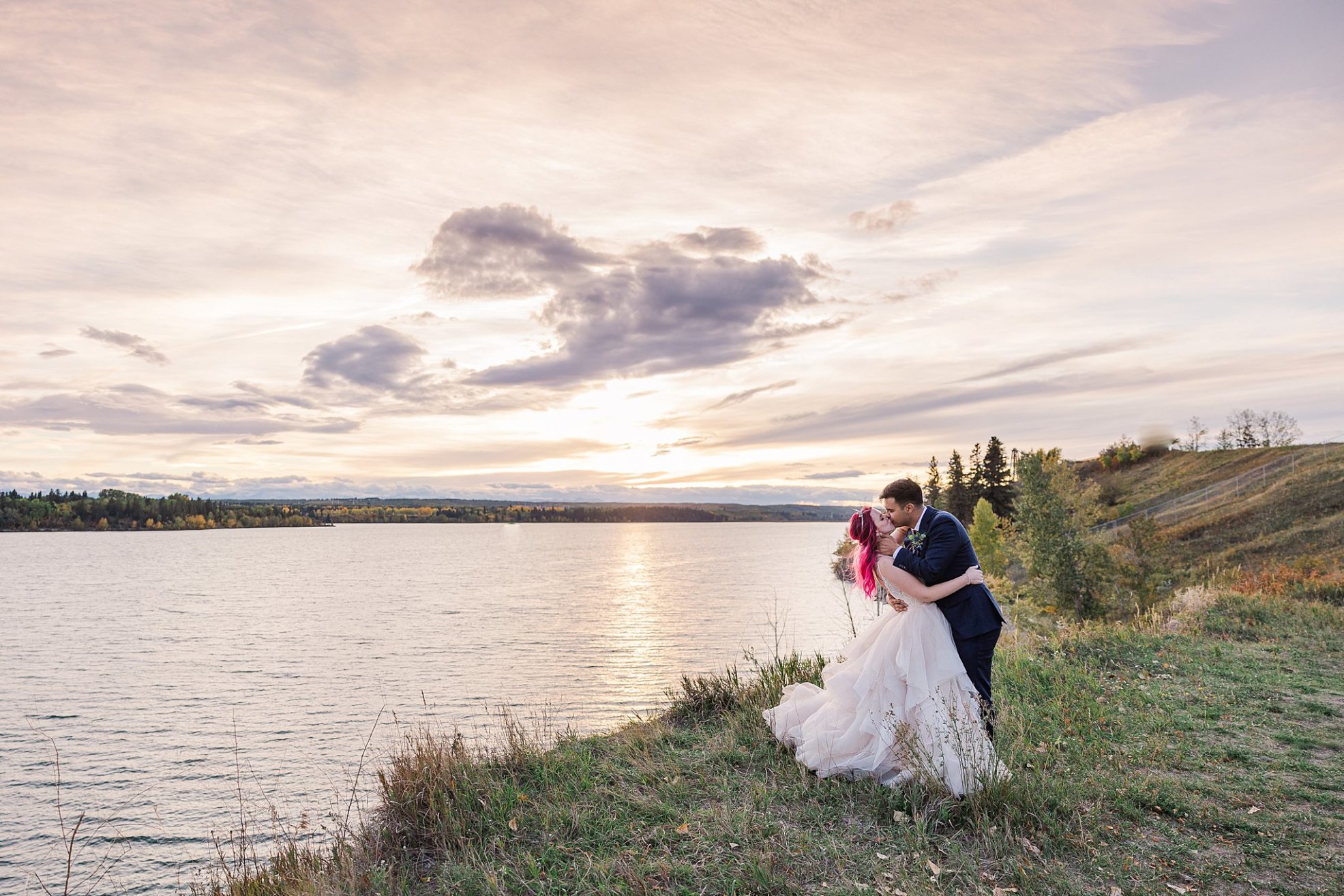 Bride and Groom kissing over a romantic sunset at the hilltop lake of Heritage Park in Calgary