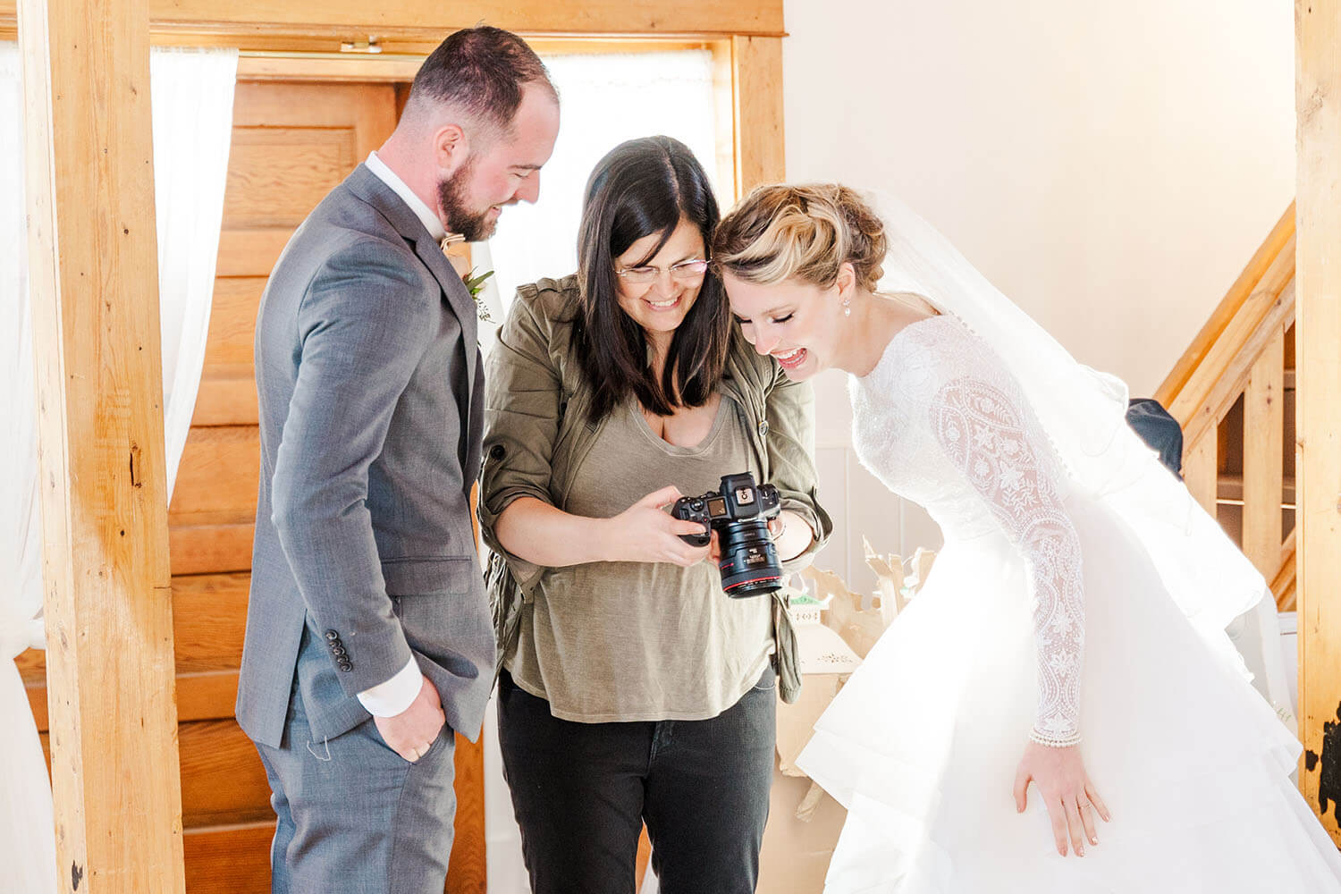 Kali wedding photographer checking the back of her camera with bride and groom looking on